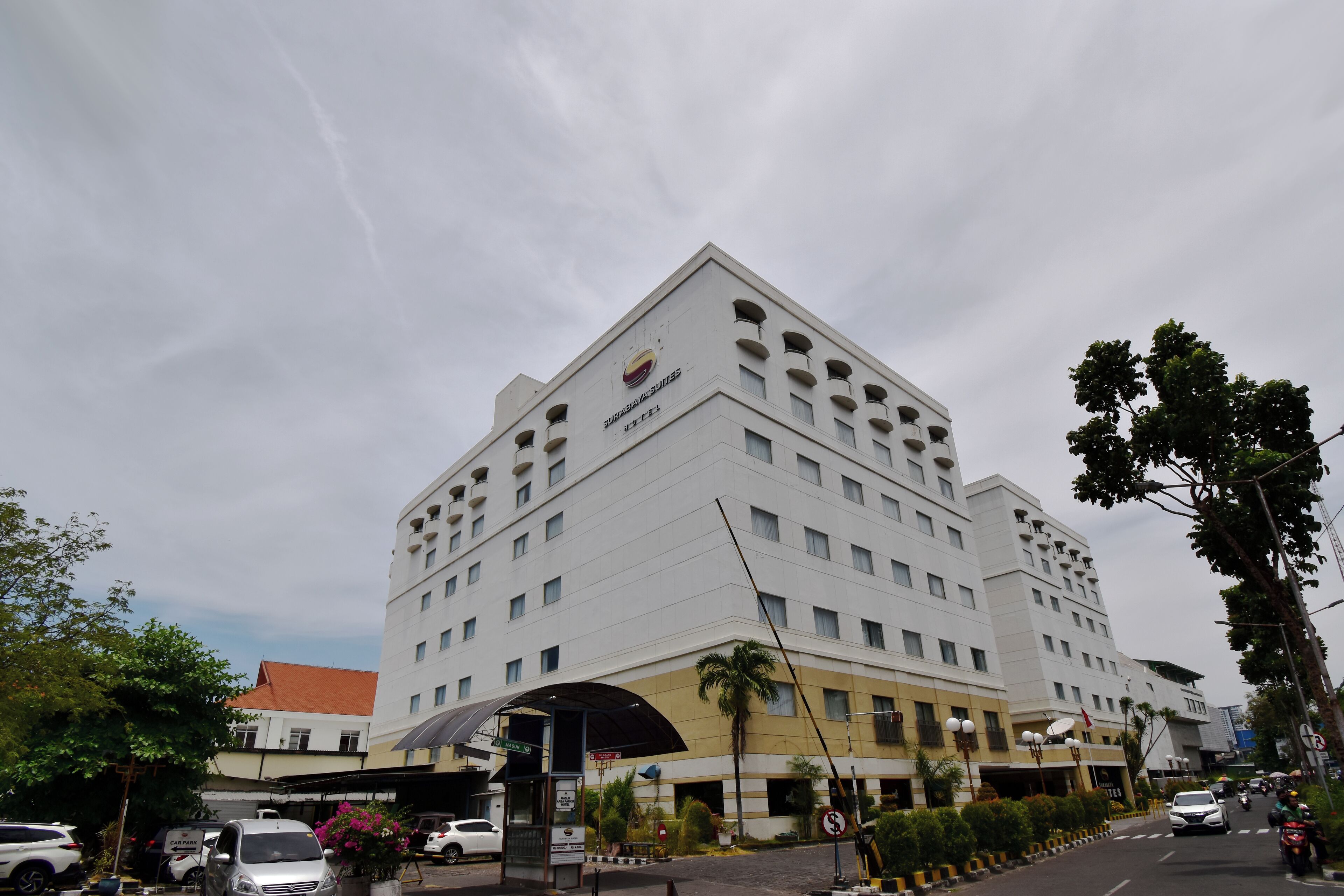 A multi-story hotel with a prominent sign, a covered entrance, and a parking area with cars and motorcycles.