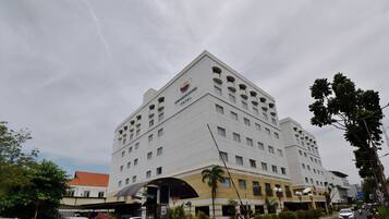 A multi-story hotel with a prominent sign, a covered entrance, and a parking area with cars and motorcycles.