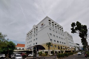 Ein mehrstöckiges Hotel mit auffälliger Beschilderung, einem überdachten Eingang und einem Parkplatz mit Autos und Motorrädern.