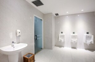 Un baño moderno con un lavamanos, una puerta de cristal y tres inodoros.