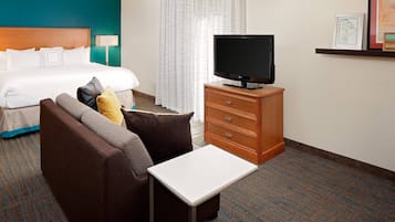 A hotel room with a bed, a TV on a wooden dresser, a sofa, and a small table.