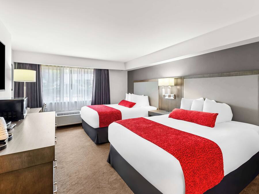 A hotel room with two beds, a desk, a TV, and a window with curtains.