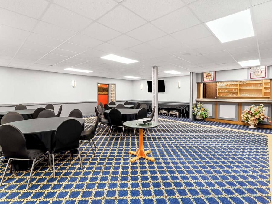 Una sala de conferencias con mesas y sillas, una alfombra estampada y una zona de recepción con mostrador y plantas decorativas.