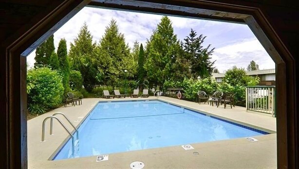 A swimming pool with lounge chairs and a view of trees. - Best Western Cowichan Valley Inn (Duncan)