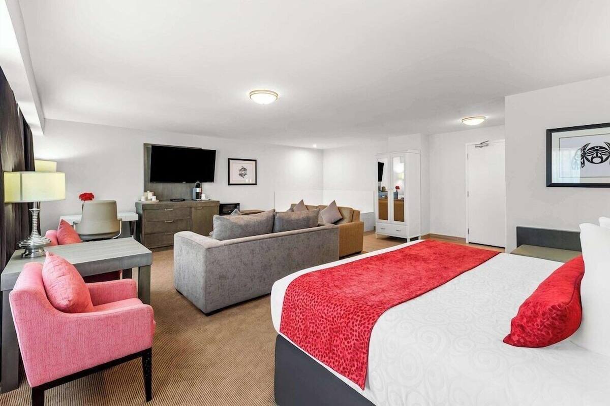 Quarto de hotel com cama, sofá, escrivaninha, televisão e espelho.