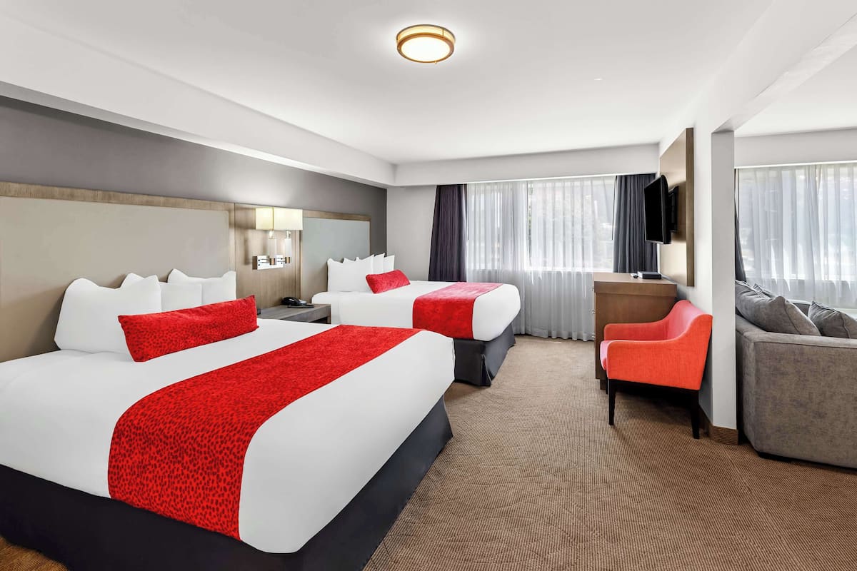 Quarto de hotel com duas camas, uma escrivaninha, uma cadeira e uma televisão.