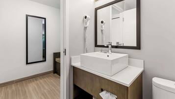 A modern bathroom with a white sink, a large mirror, and a hairdryer on the wall.
