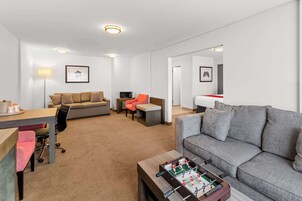 Una habitación de hotel moderna con un sofá gris, una mesa de futbolín, un televisor pequeño y un escritorio con una silla.