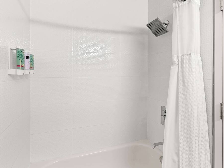 A modern bathroom with a white bathtub, a shower with a handheld showerhead, and a white shower curtain.