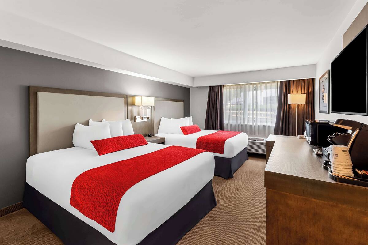 Quarto de hotel com duas camas, uma escrivaninha, uma televisão e uma janela com cortinas.