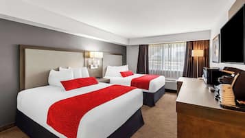 A hotel room with two beds, a desk, a TV, and a window with curtains.
