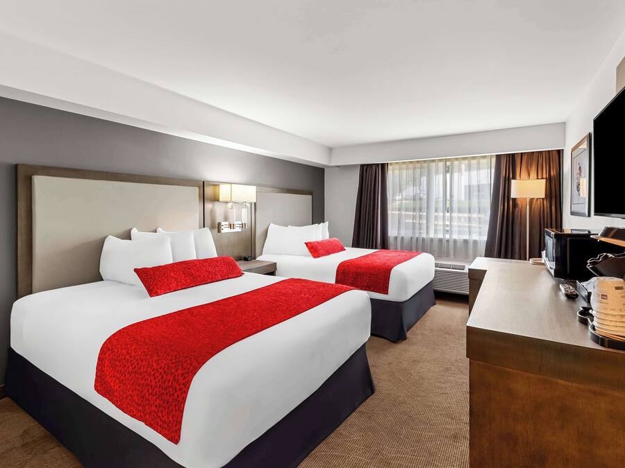 Habitación de hotel con dos camas, un escritorio, un televisor y una ventana con cortinas.