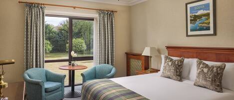 Een hotelkamer met een groot bed, twee fauteuils, een kleine tafel, een lamp en een landschapsschilderij.