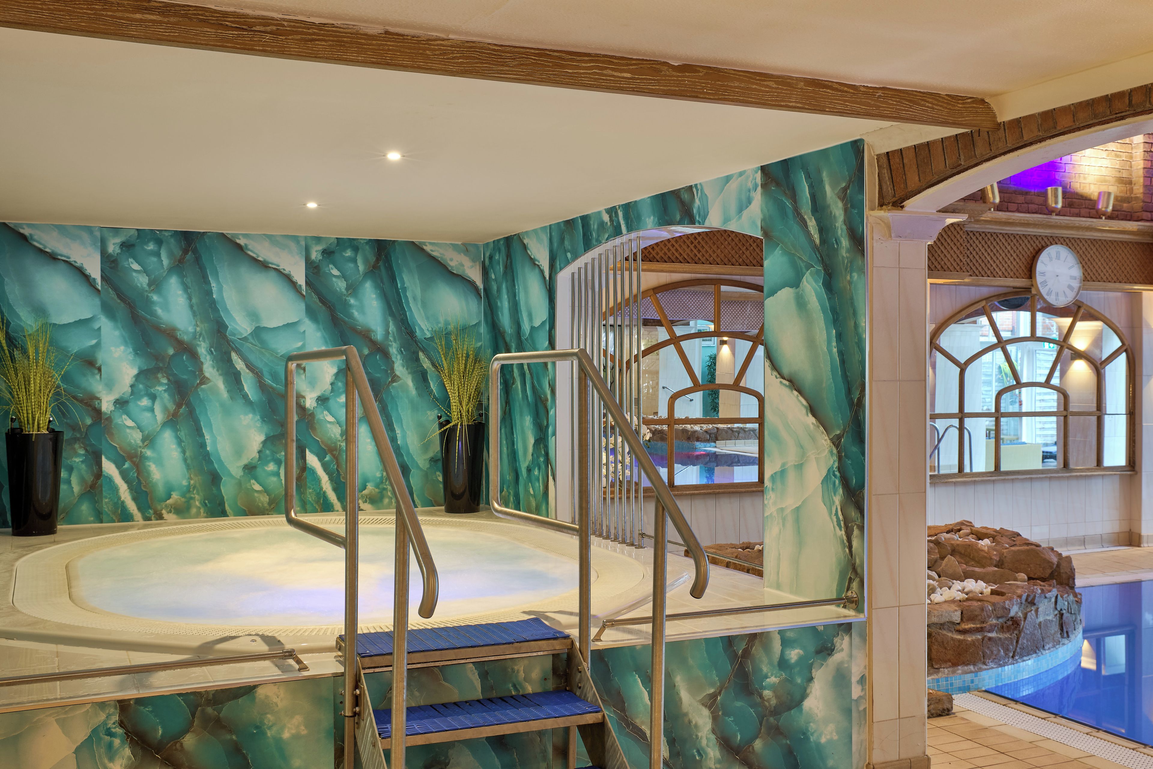 Un área de jacuzzi con un fondo de pared de mármol, una escalera de madera y una piscina con un reloj.