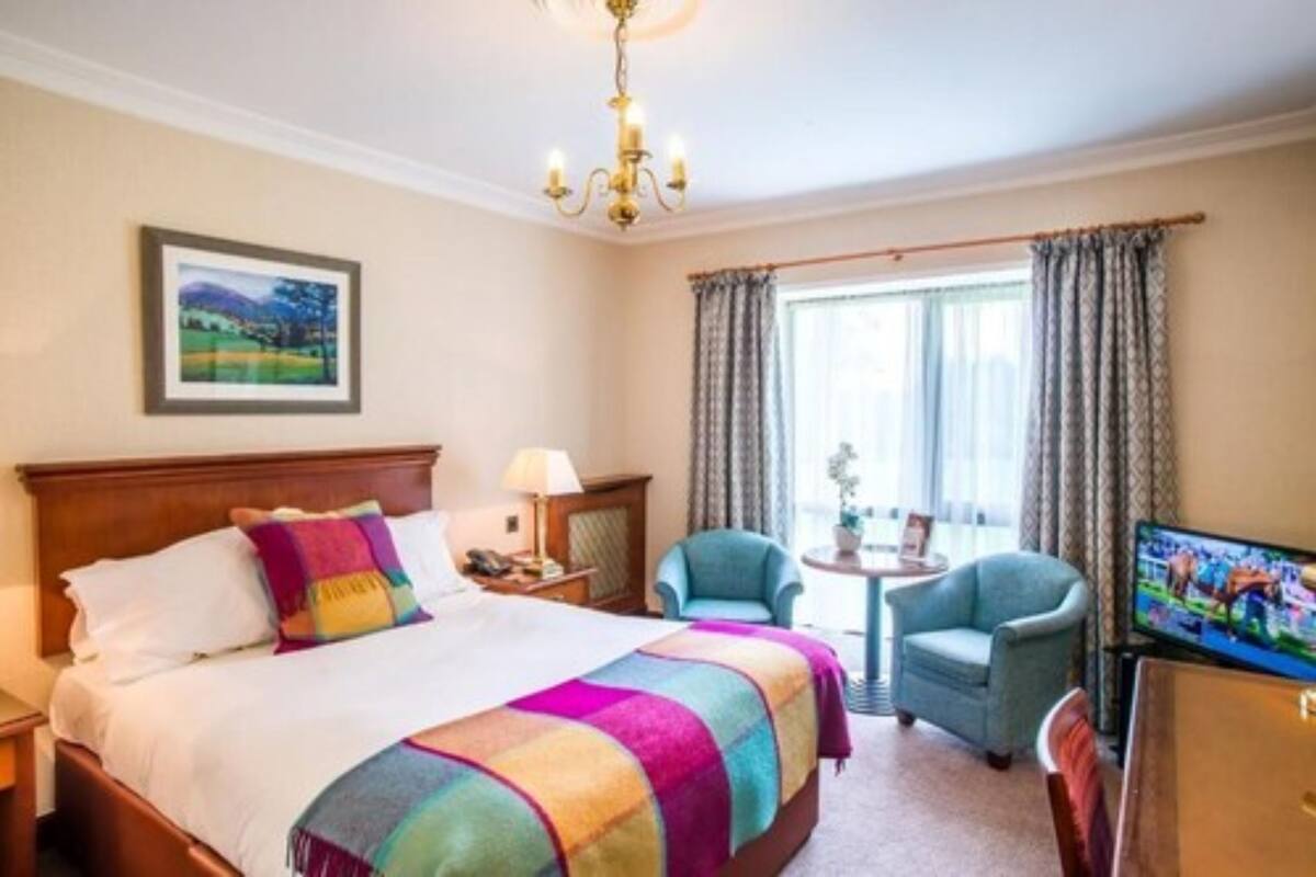 Habitación de hotel con una cama grande, televisión, una silla y un ventanal con cortinas.
