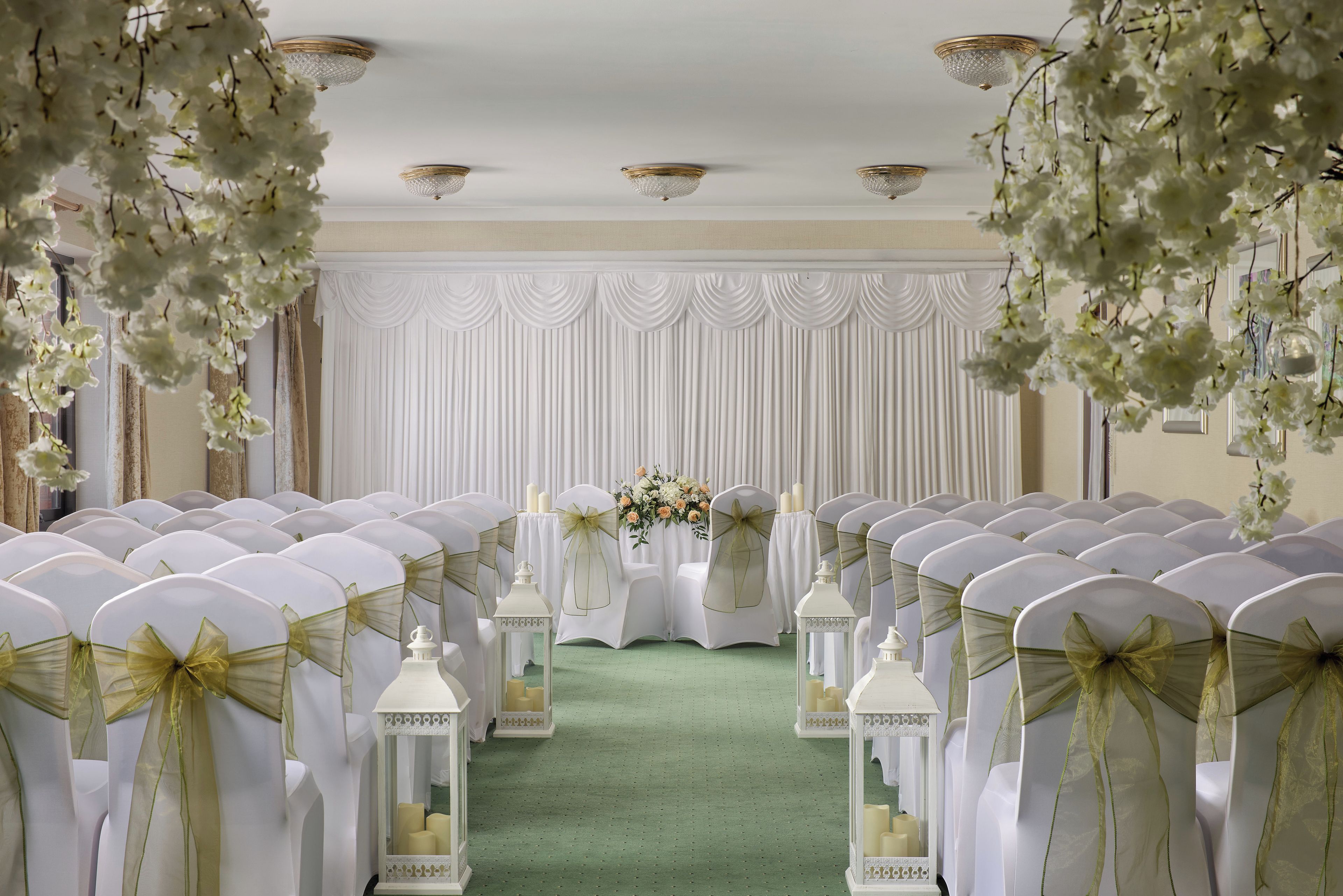 A formal event space with rows of chairs, a green carpet, and white drapery.