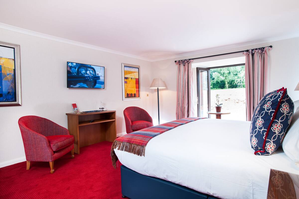 Una habitación de hotel con una cama grande, un escritorio, dos sillas, un televisor y una ventana con cortinas.