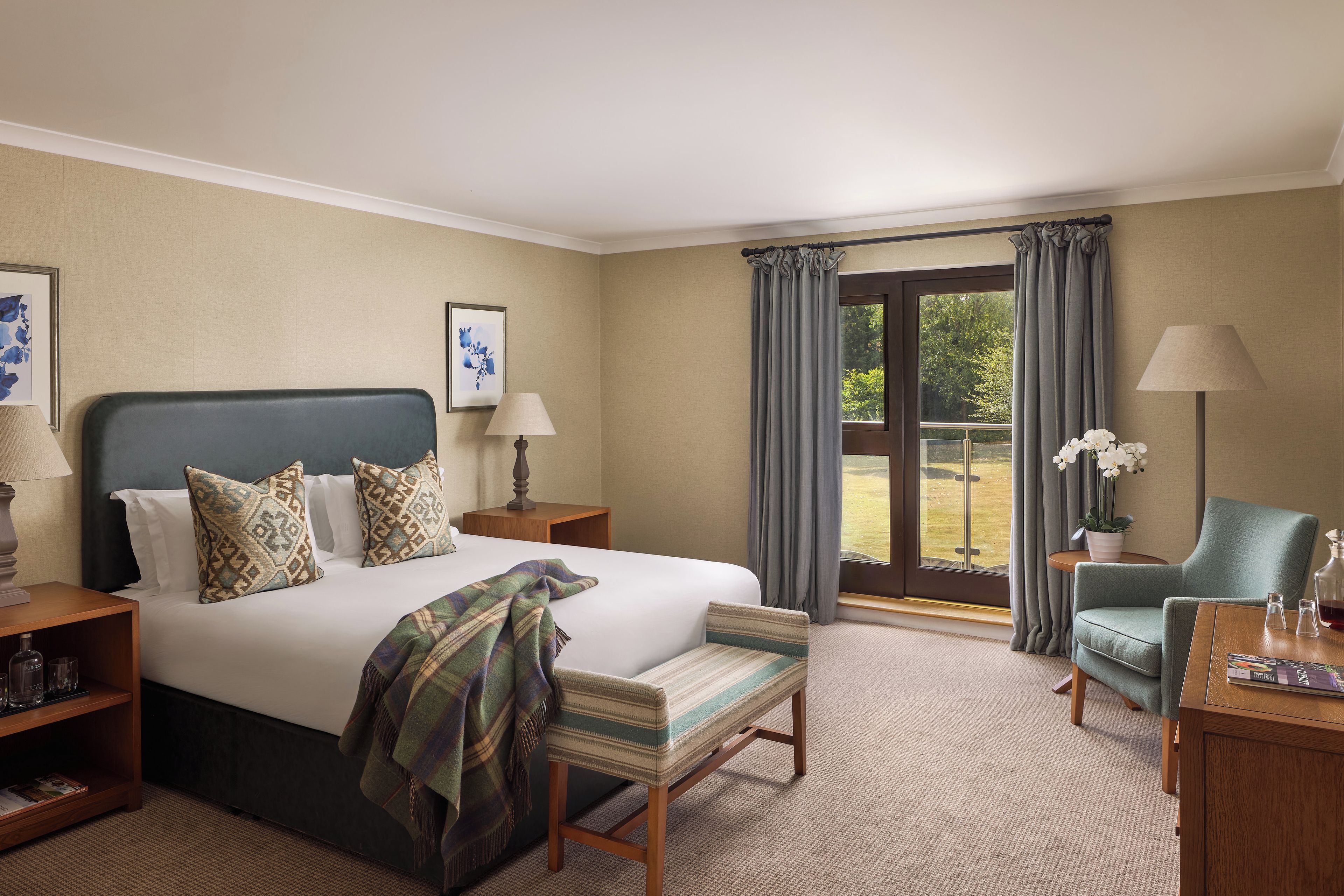 A hotel room with a large bed, a chair, a desk, and a view of the outdoors.