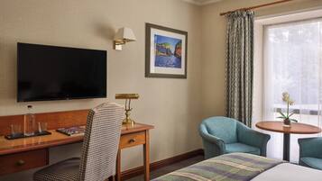 Habitación de hotel con cama, escritorio con silla, televisor, un cuadro en la pared y ventana con cortinas.