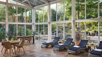 Ein Wintergarten mit großen Fenstern, einem Essbereich und Lounge-Sesseln.