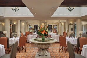 Un comedor de hotel con mesas redondas, sillas y una urna decorativa central.