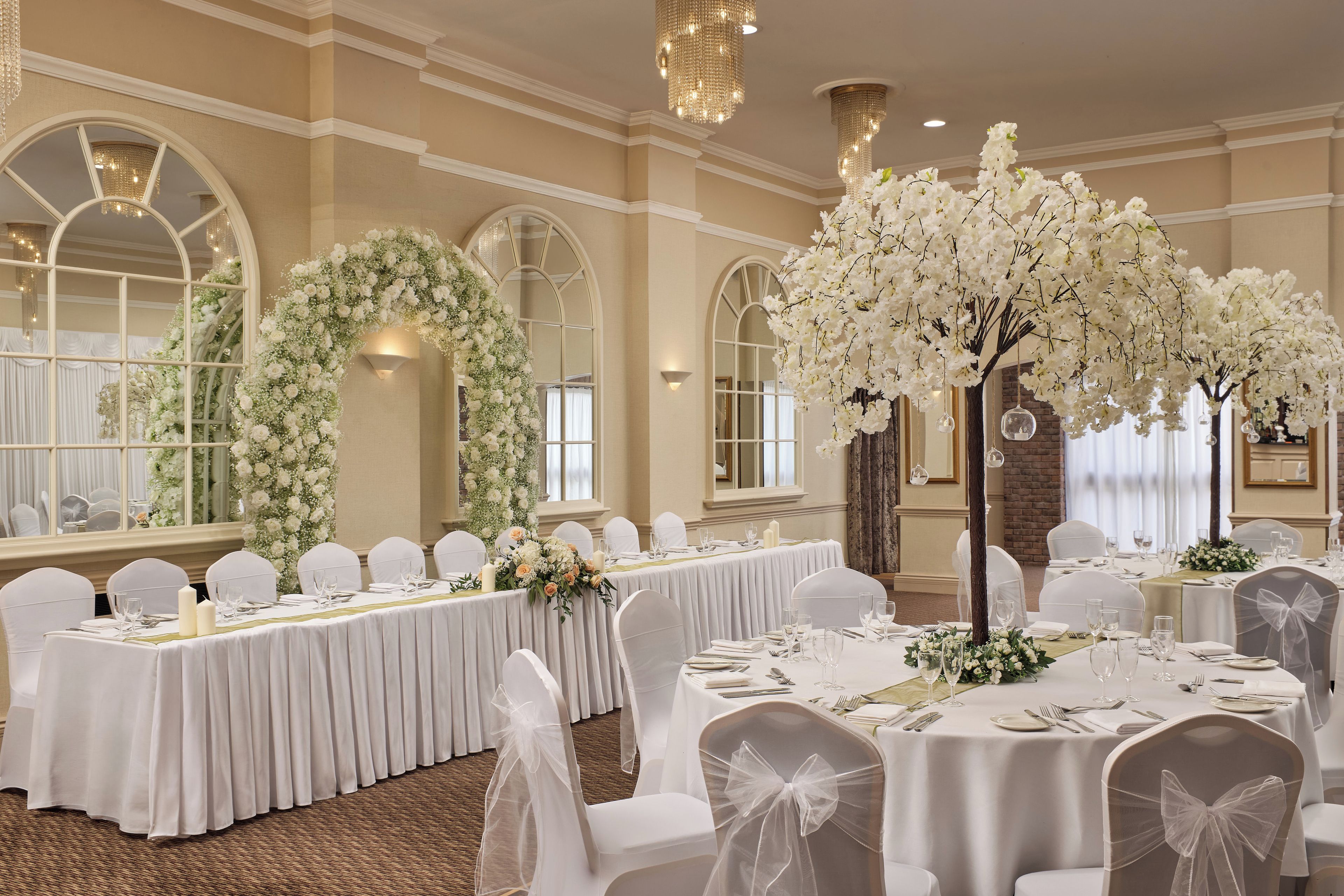 A banquet hall with round tables, white chairs, and floral decorations.
