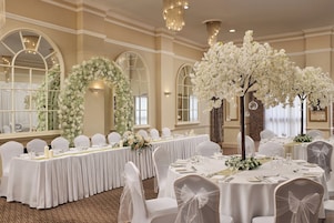 Een balzaal met ronde tafels, witte stoelen en bloemrijke decoraties.