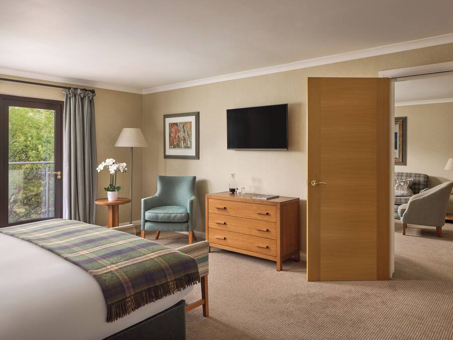 Una habitación de hotel con cama, una silla, cómoda, televisor y una puerta que da a otra habitación.