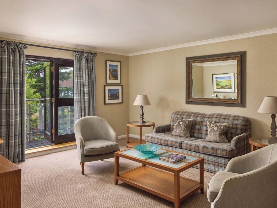 A living room with a sofa, armchairs, a coffee table, and a glass-top table with a lamp.
