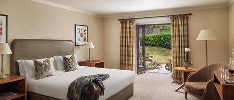 A hotel room with a large bed, two bedside tables, a chair, a small table with a lamp, and a view of the outdoors through a glass door.