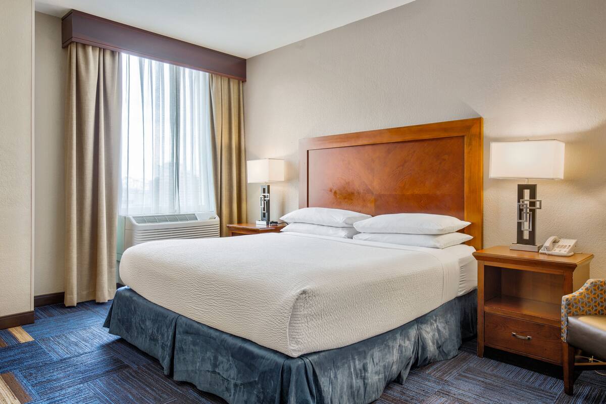Een hotelkamer met een groot bed, twee nachtkastjes, een lamp en een stoel.
