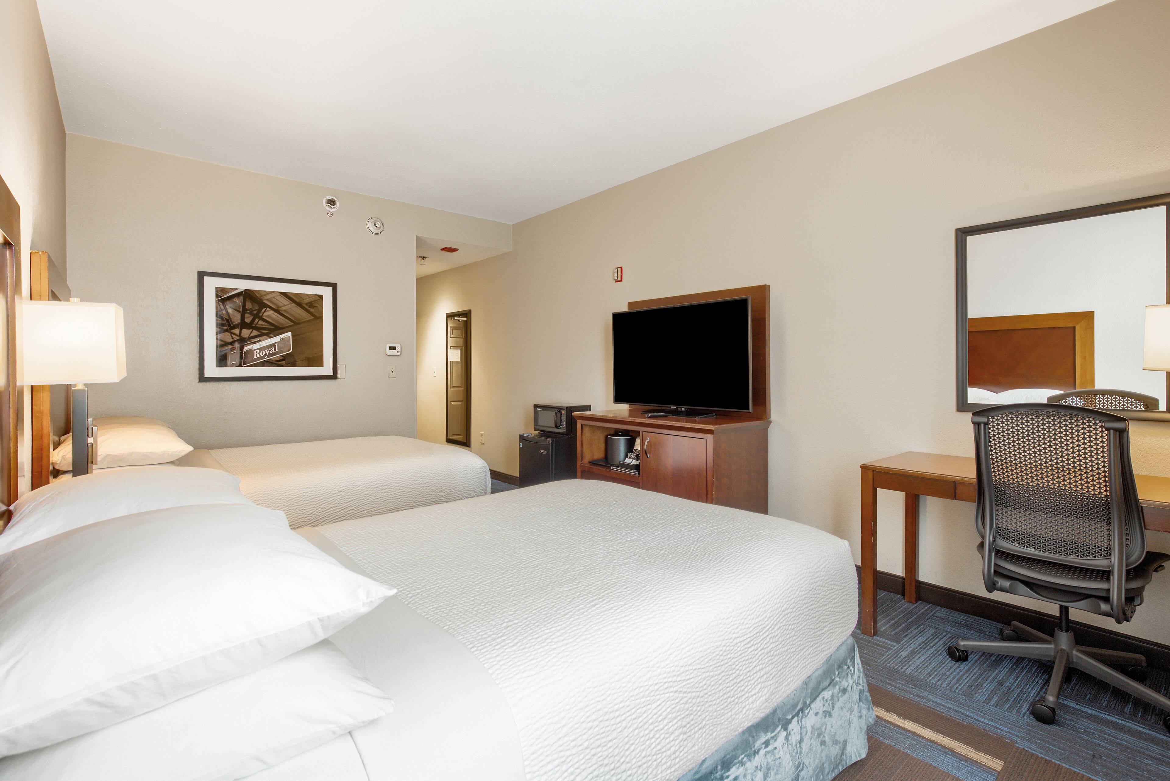 Habitación de hotel con dos camas, un escritorio, una silla, un televisor y un cuadro en la pared.