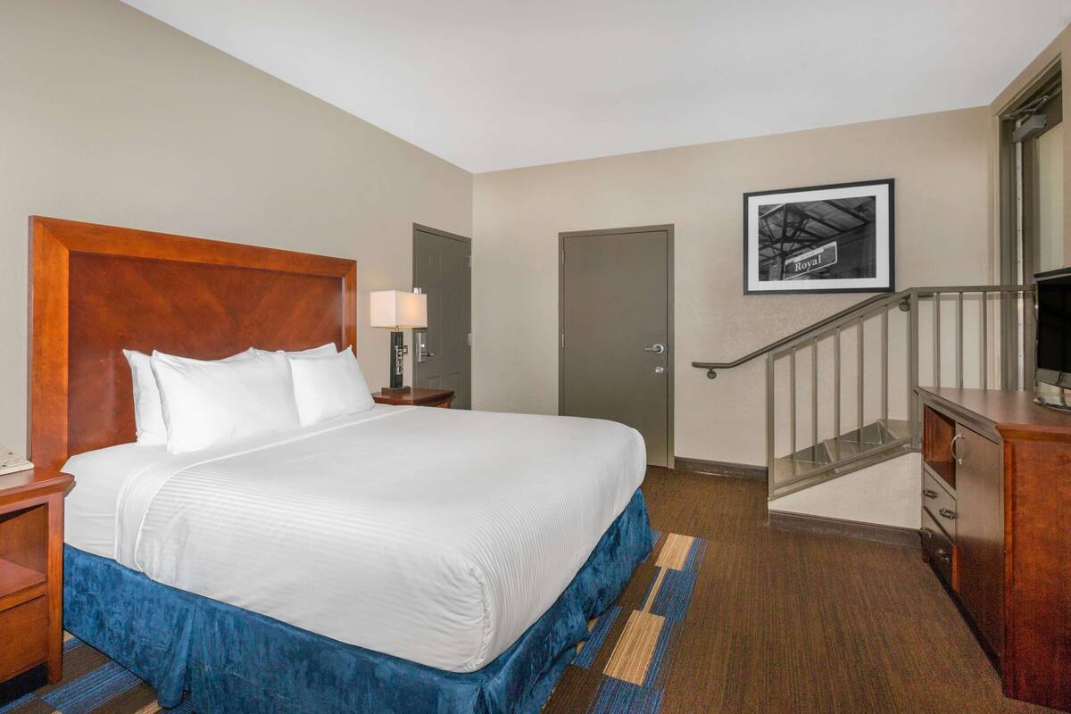 Een hotelkamer met een groot bed, een nachtkastje, een bureau, een dressoir, een deur en een trap.