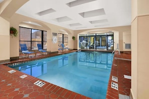 An indoor swimming pool with clear water, blue lounge chairs, and a view of the city through large windows. - Wyndham New Orleans - French Quarter (New Orleans)