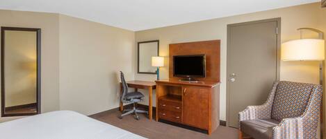 A hotel room with a bed, desk, chair, TV, and a door.