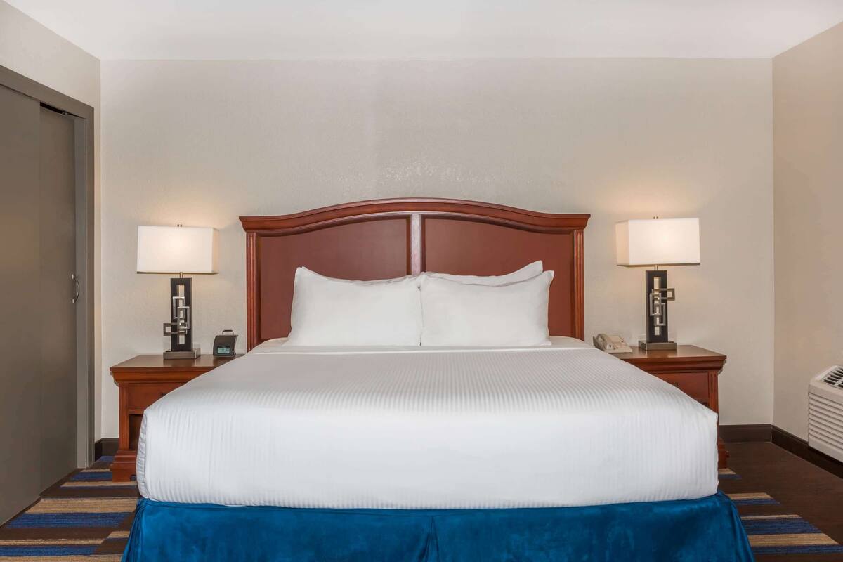 Een hotelkamer met een groot bed, twee nachtkastjes met lampen, een klok en een telefoon.
