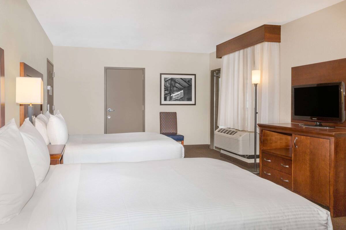 Een hotelkamer met twee bedden, een televisie, een bureau met een lamp, een stoel en een lijst aan de muur.