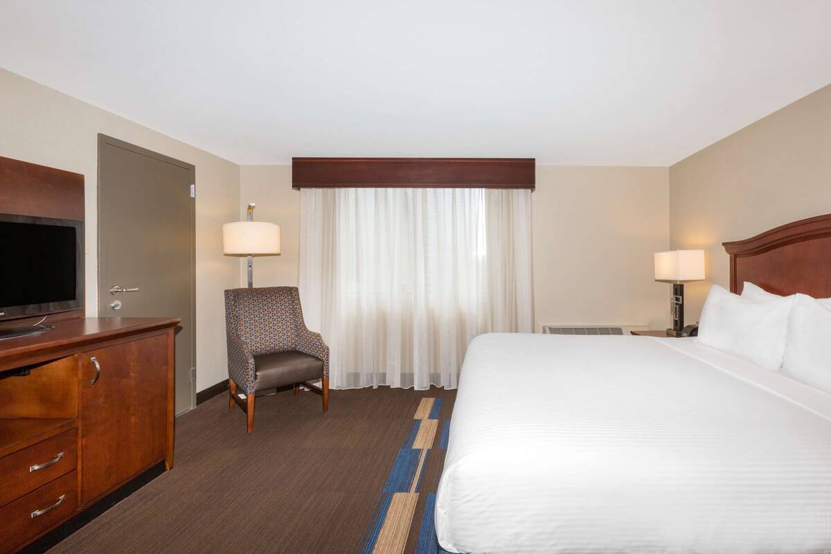 Een hotelkamer met een bed, een televisie, een stoel, een bureau en een raam met gordijnen.