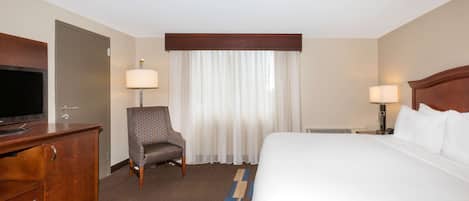 A hotel room with a bed, a TV, a chair, a desk, and a window with curtains.
