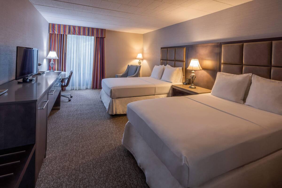 Une chambre d’hôtel avec deux lits, un bureau avec une télévision et une chaise.