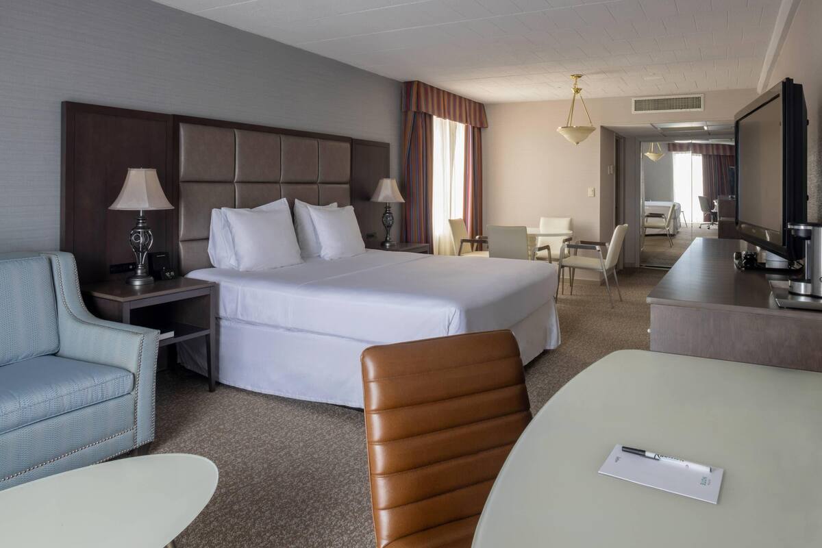 Une chambre d’hôtel avec un grand lit, un bureau avec une chaise, un canapé, une télévision et une lampe.