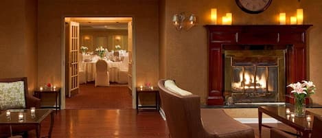 Vestíbulo de hotel con chimenea, comedor y zona de estar con sofá y mesa.