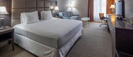 Une chambre d’hôtel avec un grand lit, un bureau avec une télévision, une chaise, une petite table et un canapé.