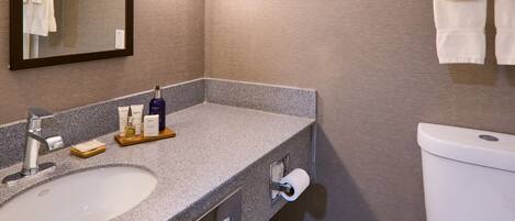 Ein Badezimmer mit Granitplatte, Waschbecken, Spiegel, Toilette und Handtuchhalter.