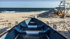 Un bote en una playa arenosa con una torre de salvavidas al fondo.