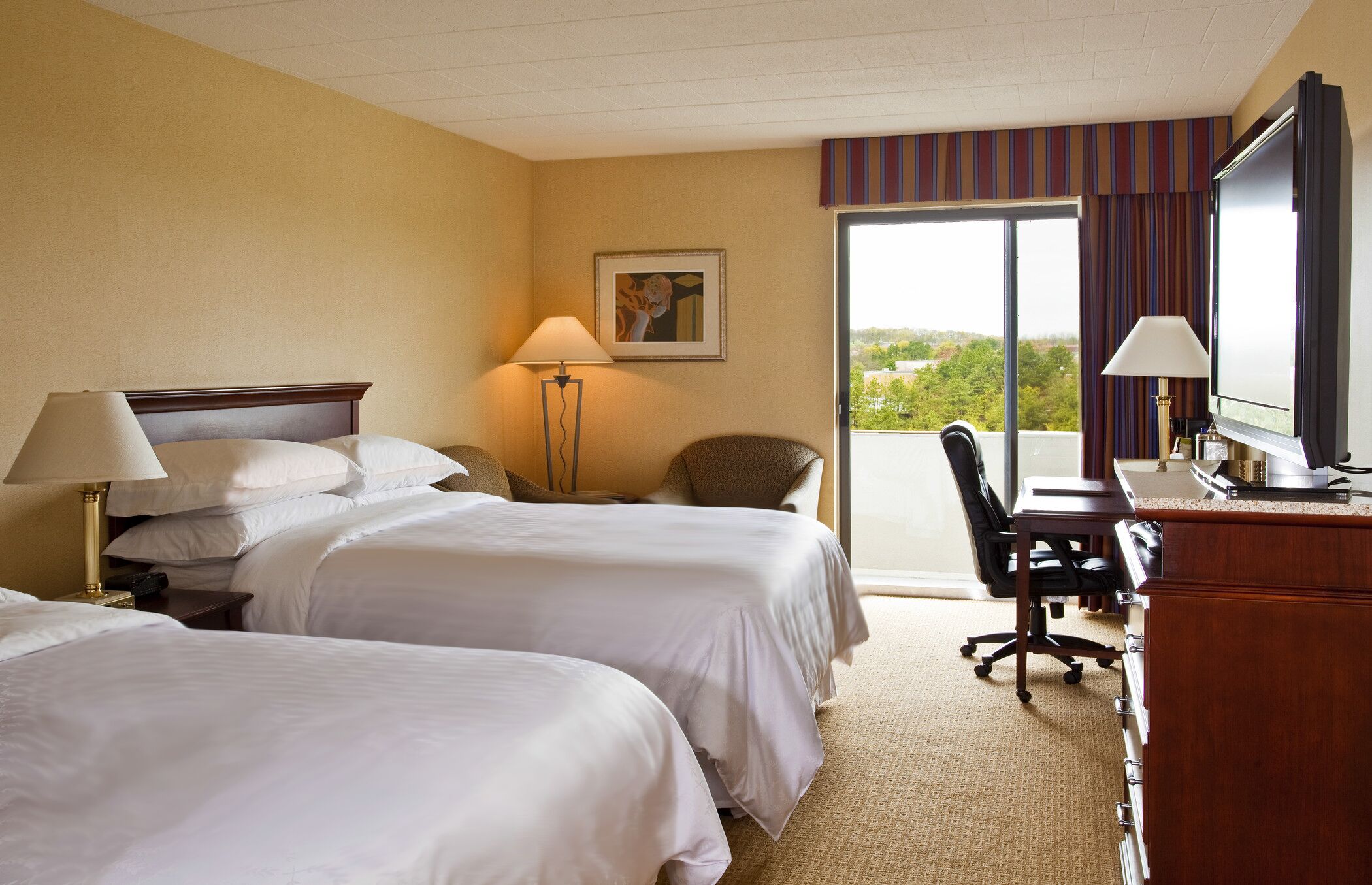 A hotel room with two beds, a desk, a chair, a TV, and a window with a view.