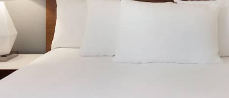 A neatly made bed with white linens and pillows, a wooden headboard, and a bedside lamp.