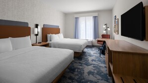 A hotel room with two beds, a desk, a chair, a TV, and a window with curtains.