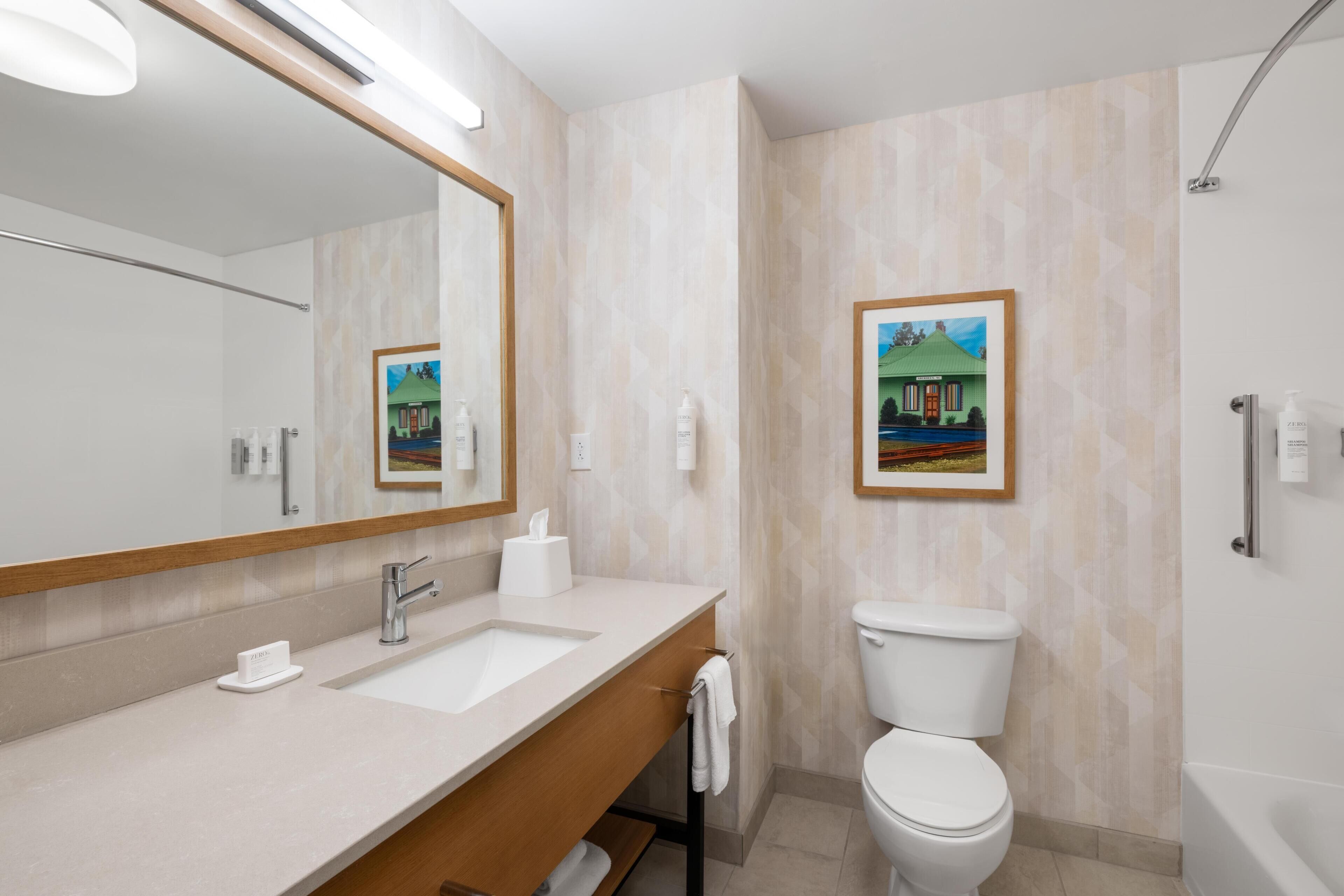 A modern bathroom with a large mirror, a sink, a toilet, and a bathtub.