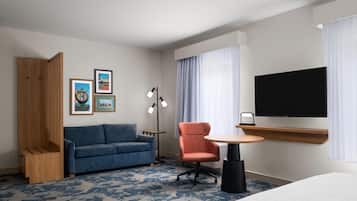 A hotel room with a blue sofa, a wooden cabinet, a round table, a TV, and artwork on the wall.